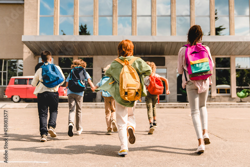 Tableau sur toile Little kids schoolchildren pupils students running hurrying to the school building for classes lessons from to the school bus