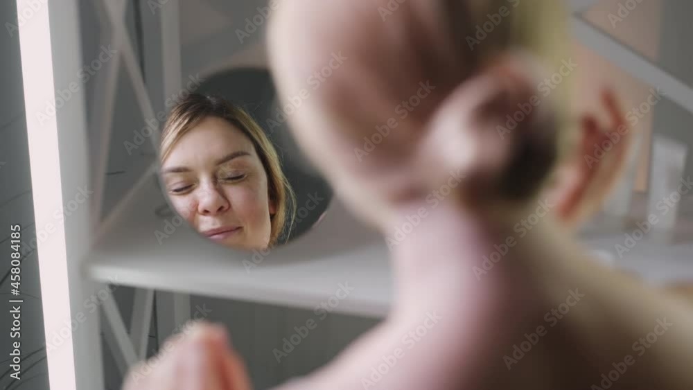 Facial care. Skin treatment. Anti-aging hydration. Morning routine. Pretty middle age woman looking in mirror applying moisturizing cream on perfect clean face after shower.