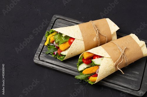 Tortilla wraps, with breaded chicken sticks with vegetables, burritos, on a black background,  horizontal, no people, photo