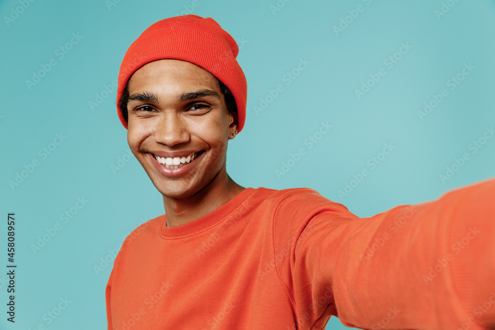 Close up young smiling happy african american man 20s in orange shirt hat doing selfie shot pov on mobile phone isolated on plain pastel light blue background studio portrait People lifestyle concept Close up young smiling happy african american man 20s in orange shirt hat doing selfie shot pov on mobile phone isolated on plain pastel light blue background studio portrait People lifestyle concept
