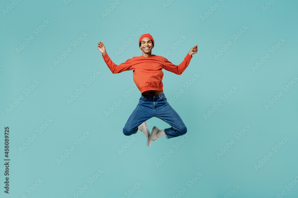 Full body young happy african american man in orange shirt hat hold spread hands in yoga om aum gesture relax meditate try calm down jump high isolated on plain pastel light blue background studio.