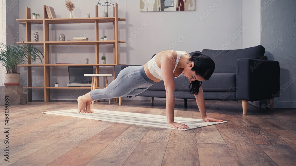 Brunette sportswoman standing in plank on fitness mat at home
