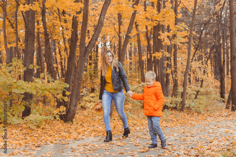 Mother and son walking in the fall park and enjoying the beautiful autumn nature. Season, single parent and children concept. Mother and son walking in the fall park and enjoying the beautiful autumn nature. Season, single parent and children concept.