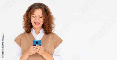 Curly smiling young woman demonstrating white teeth using cell phone, messaging, being happy to text with her boyfriend, looking at screen of smartphone. Modern technologies and communication