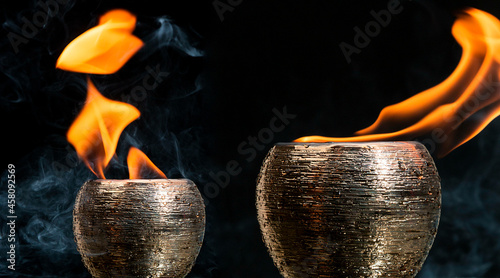 Potes dourados de cerâmica saindo fogo de dentro envolvido por fumaça em um fundo preto.  photo
