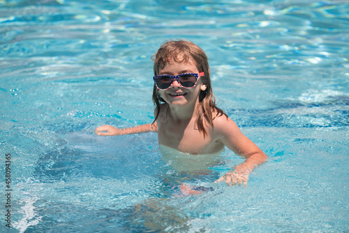 Child boy swim in swimming pool. Summertime and swimming activities for children on the pool. Portrait of cute kid boy in sunglasses in pool in sunny day. Funny kids face.