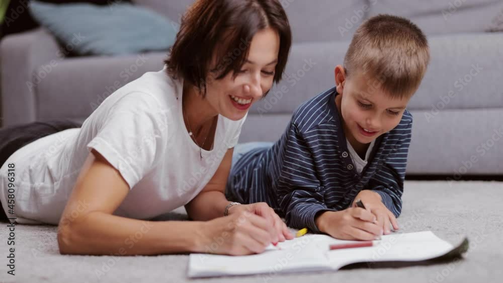 Loving caucasian mother lying on floor with little son and drawing in white album with colorful pencils. Family weekend and children creativity concept. Loving caucasian mother lying on floor with little son and drawing in white album with colorful pencils. Family weekend and children creativity concept.