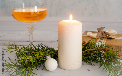 Scena festiva con una candela bianca accesa e una pallina di natale acanto con un ramo di abete dietro e un bicchiere di champagne e un pacchetto regalo sullo sfondo. Feste. Nuovo Anno. Dicembre. 