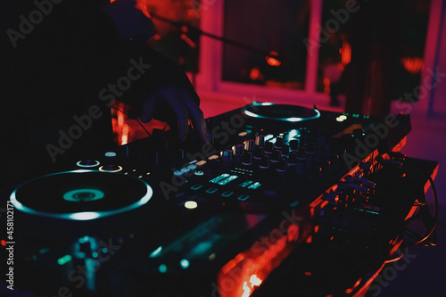 Techno music dj playing electronic musical tracks with turntables and sound mixer on stage in night club in neon red lights. Professional disc jockey plays music in nightclub