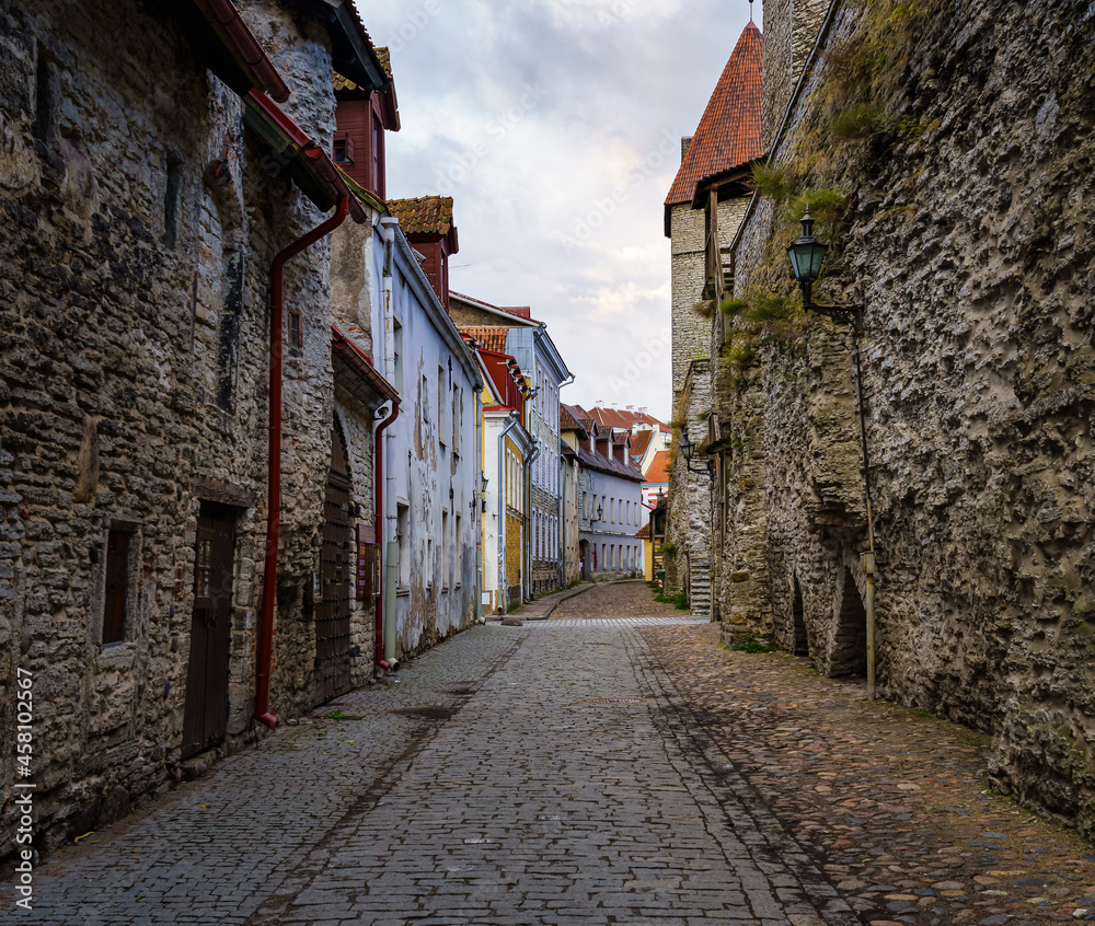 Cobbled alley with medieval houses and stone wall in Tallinn Estonia.