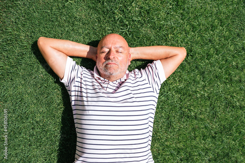 Retired man resting on his back on grass with hands on head with grass background. © Margalliver