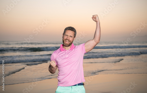 successful guy on sunrise beach. bearded man in shirt. celebrate success. summer vacation