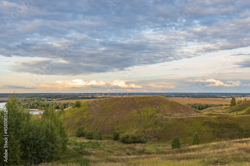 The vibrant colors of the sunset over the hill. Colorful landscape in the evening, gorgeous blue sky with golden clouds over a field with hills and a river. A magical moment of nature.