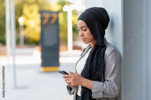Side view of a muslim adult woman using phone looking down in the park