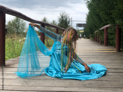little girl plays the character elsa from the cartoon frozen outside. pigtailed Princess in a blue dress poses with her eyes closed on wooden bridge photo