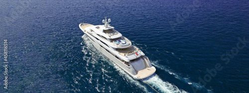 Aerial drone ultra wide panoramic photo of beautiful modern super yacht with wooden deck cruising in high speed deep blue open ocean sea © aerial-drone