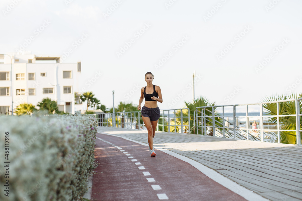 beautiful fitness girl in shorts and sports top running on the waterfront by the sea in sunny weather beautiful fitness girl in shorts and sports top running on the waterfront by the sea in sunny weather