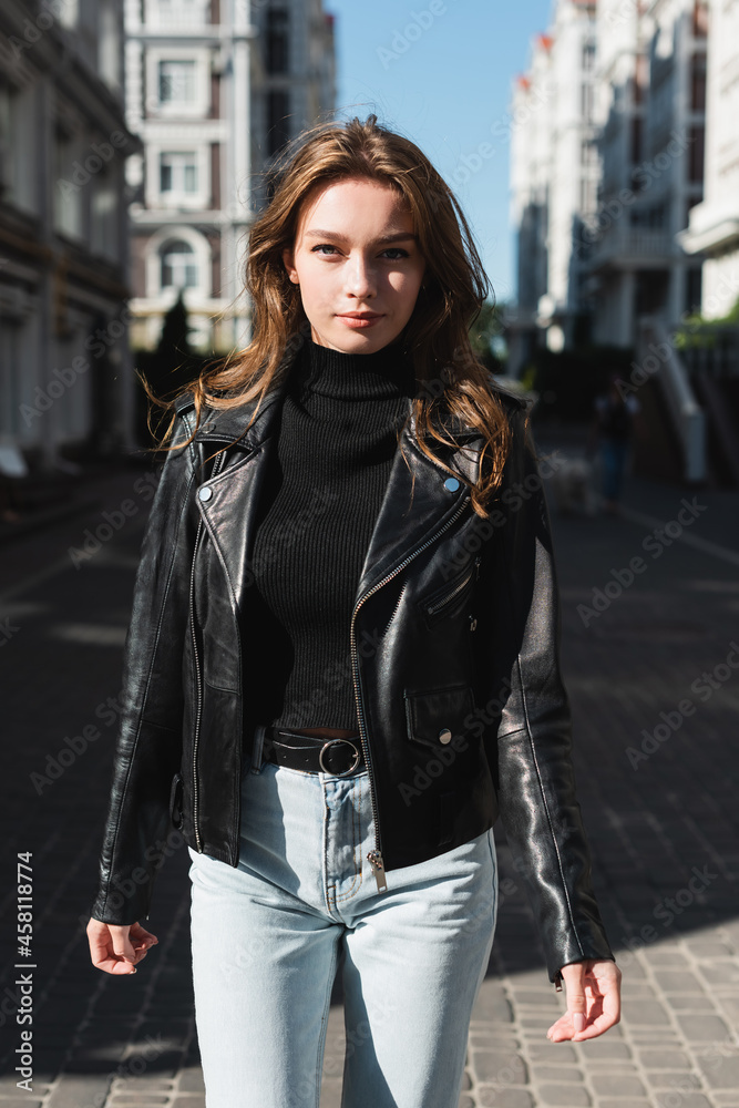 young woman in black turtleneck and leather jacket looking at camera on urban street of europe young woman in black turtleneck and leather jacket looking at camera on urban street of europe