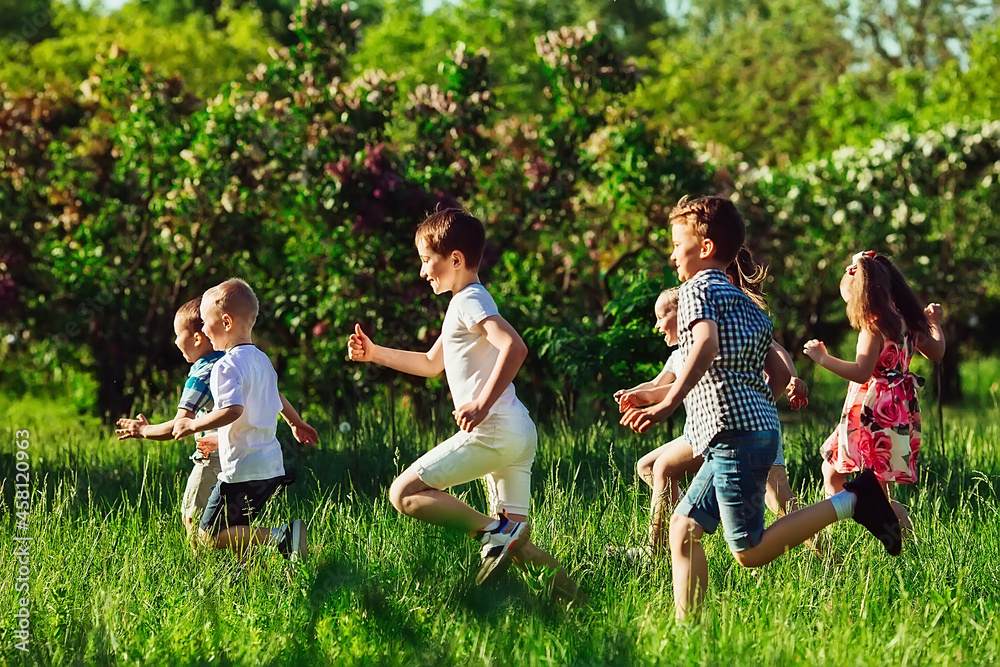 A group of happy children of boys and girls run in the Park on the grass on a Sunny summer day. A group of happy children of boys and girls run in the Park on the grass on a Sunny summer day.