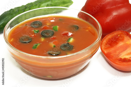 Cold soup gazpacho on in a transparent plate on a white background