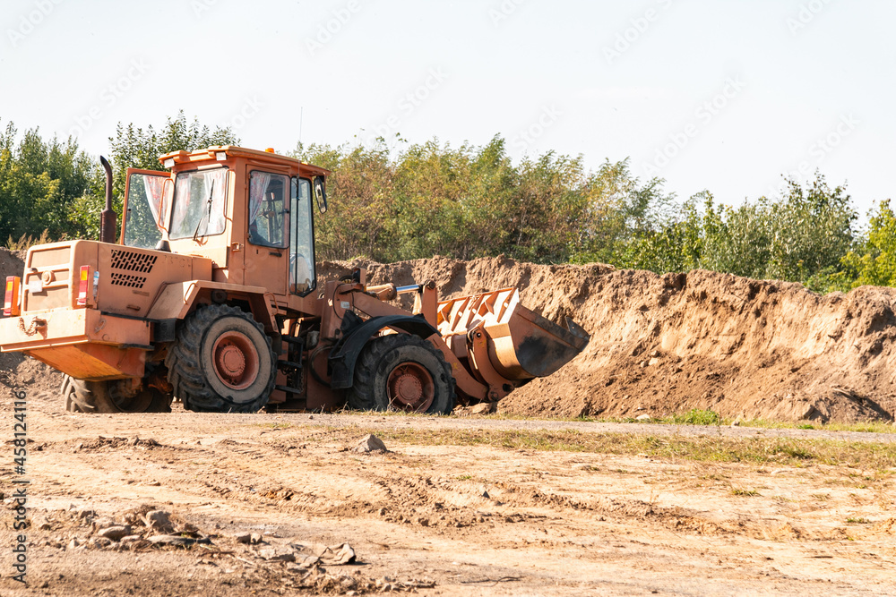 A wheeled dozer collects soil into a bucket in a quarry. Construction works.