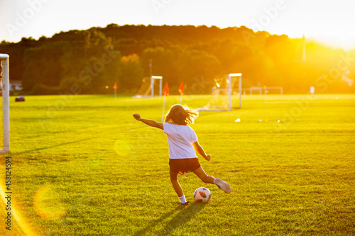 Young girl kicking a soccer ball at sunset on the soccer field  photo