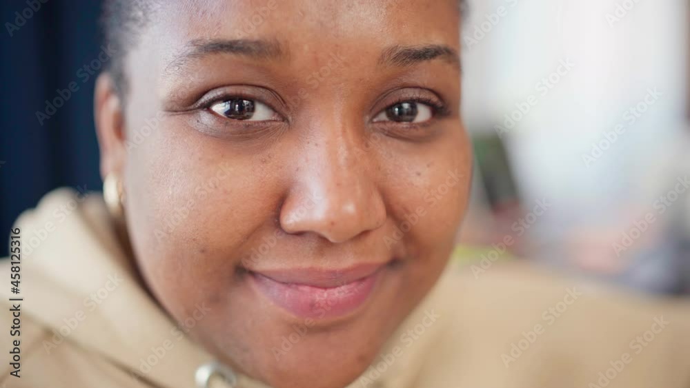 Closeup zoom in portrait of beautiful Black plus size young woman in beige hoodie looking at camera and smiling. Cheerful plump African female with brown eyes posing indoors Closeup zoom in portrait of beautiful Black plus size young woman in beige hoodie looking at camera and smiling. Cheerful plump African female with brown eyes posing indoors