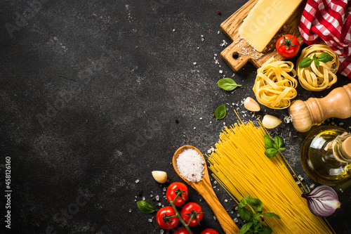 Italian food background on black. Raw Pasta, fresh tomatoes, olive oil, spices and basil. Top view with copy space.