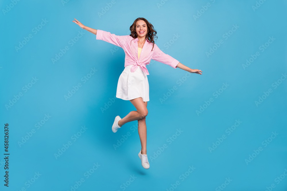 Photo of shiny pretty young woman dressed white skirt smiling having fun jumping high isolated blue color background
