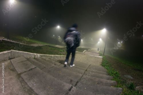 The guy walks the stairs in the night park, during the fog