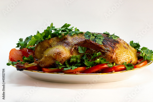 festive dish baked duck with a crispy crust garnished with slices of tomatoes and herbs on a large plate close-up on a white background