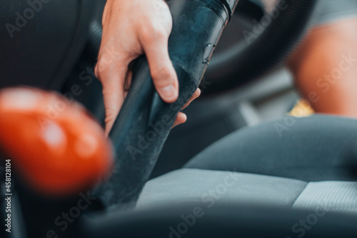 Manos de una chica joven utilizando una aspiradora para aspirar los asientos de un vehículo en el túnel de limpieza photo