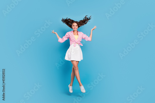 Photo of pretty cute young lady wear pink shirt jumping high rising arms hands smiling isolated blue color background