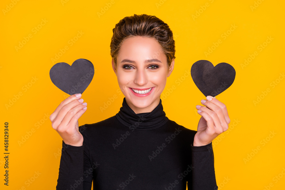 Portrait of attractive cheerful girl holding in hands two heart cards amour isolated over bright yellow color background Portrait of attractive cheerful girl holding in hands two heart cards amour isolated over bright yellow color background
