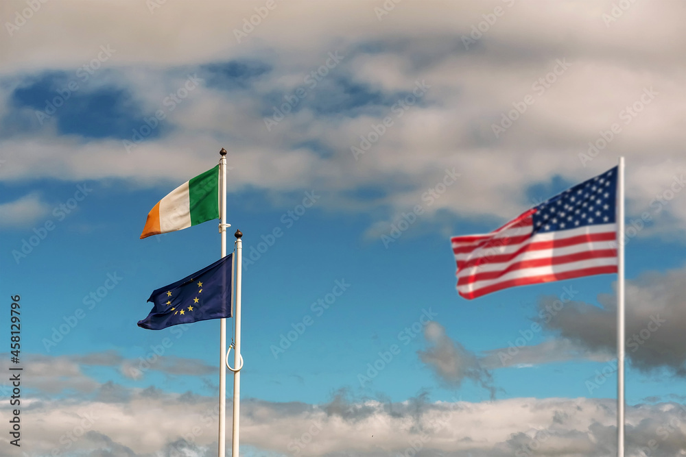 National flag of Ireland and Euro Union in focus. Waving flag of United States of America out of focus on blue color cloudy sky