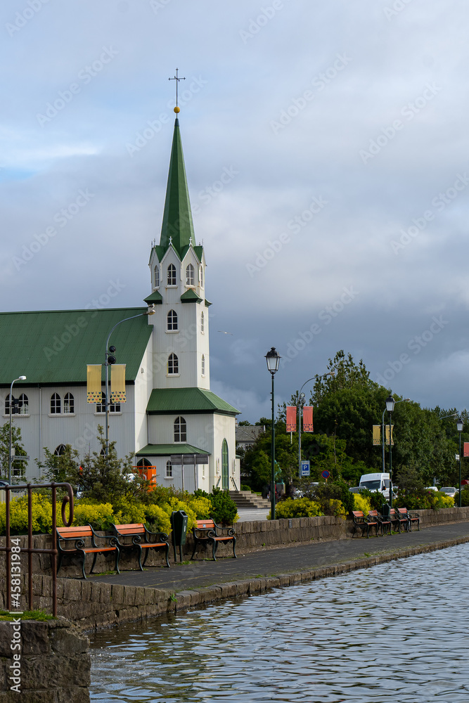 Beautiful view of the Iceland Church with white walls and green roof in front of the lake on a cloudy sky in Reykjavik, Iceland. Architecture, landmark, worship service, religion, faith concept