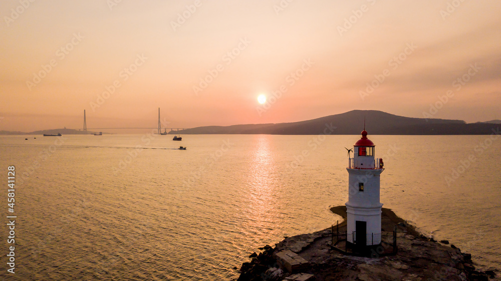 View from above. Tokarevsky lighthouse in Vladivostok at dawn. A beautiful lighthouse against the backdrop of the calm sea and the Russian bridge.