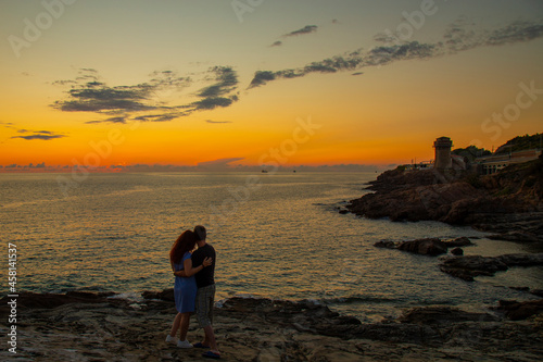 silhouettes of hugging man and woman on a mountain above the sea during sunset , in summer on vacation