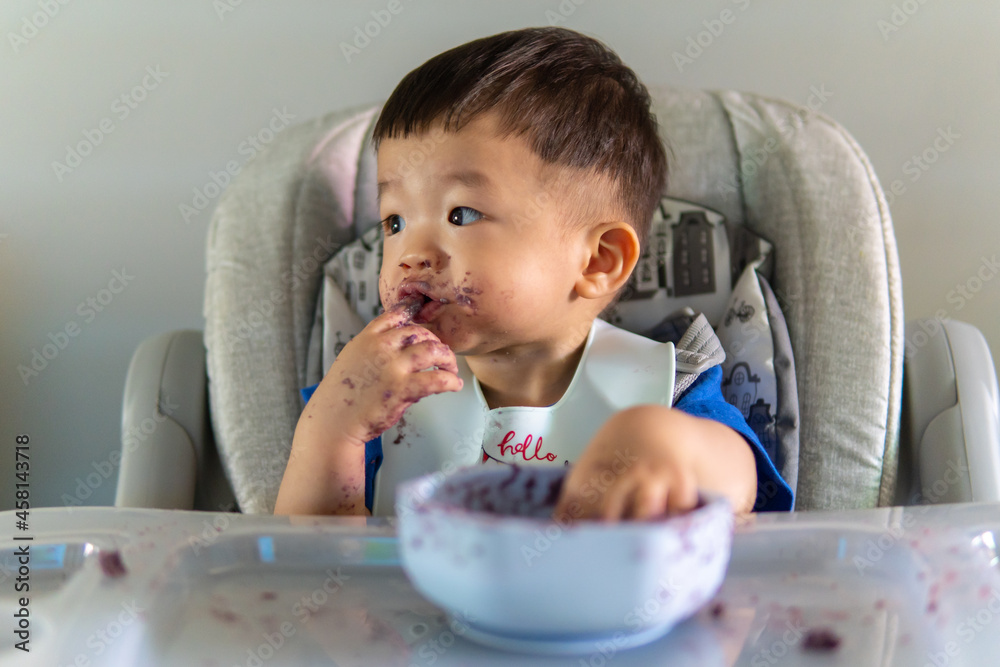 adorable and cute happy Asian Chinese baby boy siting on baby chair enjoying meal with dirty face adorable and cute happy Asian Chinese baby boy siting on baby chair enjoying meal with dirty face