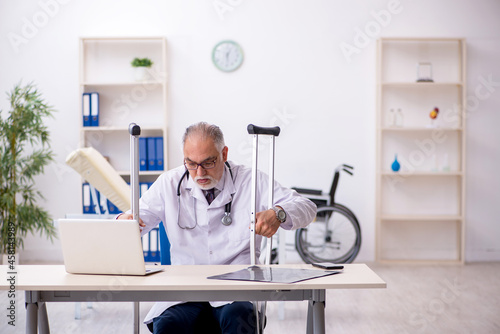 Leg injured old male doctor working in the clinic