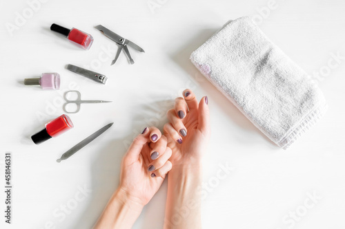 Closeup of woman hands with polished nails and manicure instruments  bottles of nail polish. caucasian woman receiving french manicure at home or at nail salon. selfcare  beauty procedures yourself