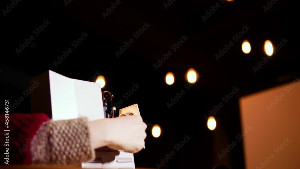 Old fashioned slide projector and young woman inserting its photo film for making ready to work. The caucasian lady is loading the image negatives into a retro cinematographic device