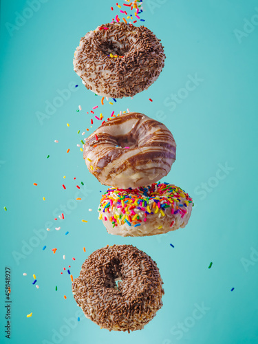 Four multi-colored donuts on a blue background. Splashes of confectionery dust. Levitation. Sweet food. Holiday symbol. Restaurant, pastry shop, culinary blog.
