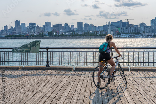 Montreal, Quebec, Canada - August 3 2021 : A woman rides a bicycle and watching the sunset in Jean-Drapeau park maritime shuttle landing stage. Saint Helens Island.