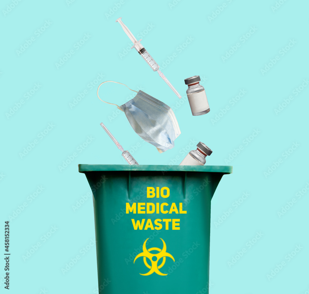 Biomedical waste concept, syringes masks and other waste thrown in garbage can with biohazard