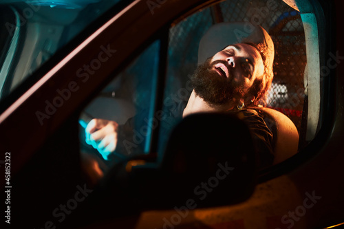 Bearded man sleeping in his vehicle illuminated by teal and orange lights