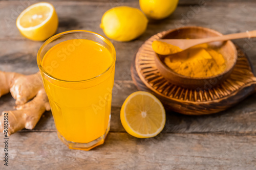 Glass of tasty juice with lemon and turmeric on wooden background