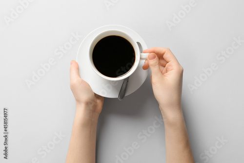 Female hands with cup of coffee on light background