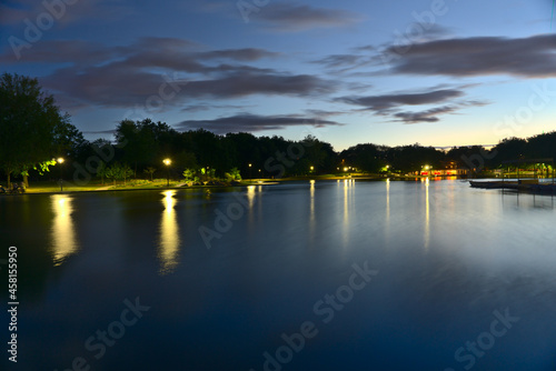 A long exposure of Beaver Lake, Mount Royal, Montreal, QC, Canada at twilight blue hour on a cloudy summer day. The lights and trees reflect on the lake.