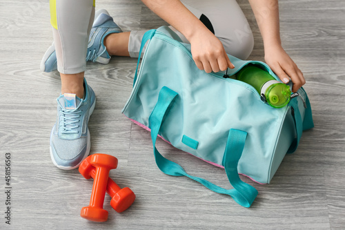 Woman in sport shoes preparing bag for training on light wooden floor photo